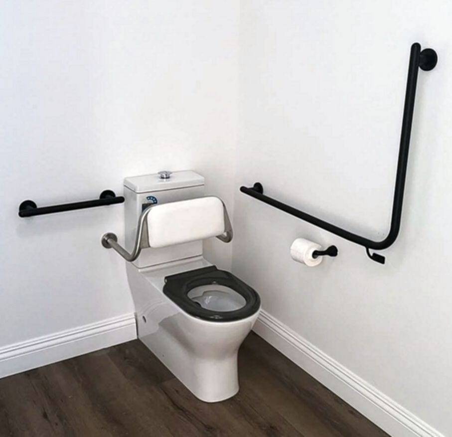 Accessible toilet with a padded backrest and a dark seat, black grab bars mounted on both walls and a matching toilet paper holder
