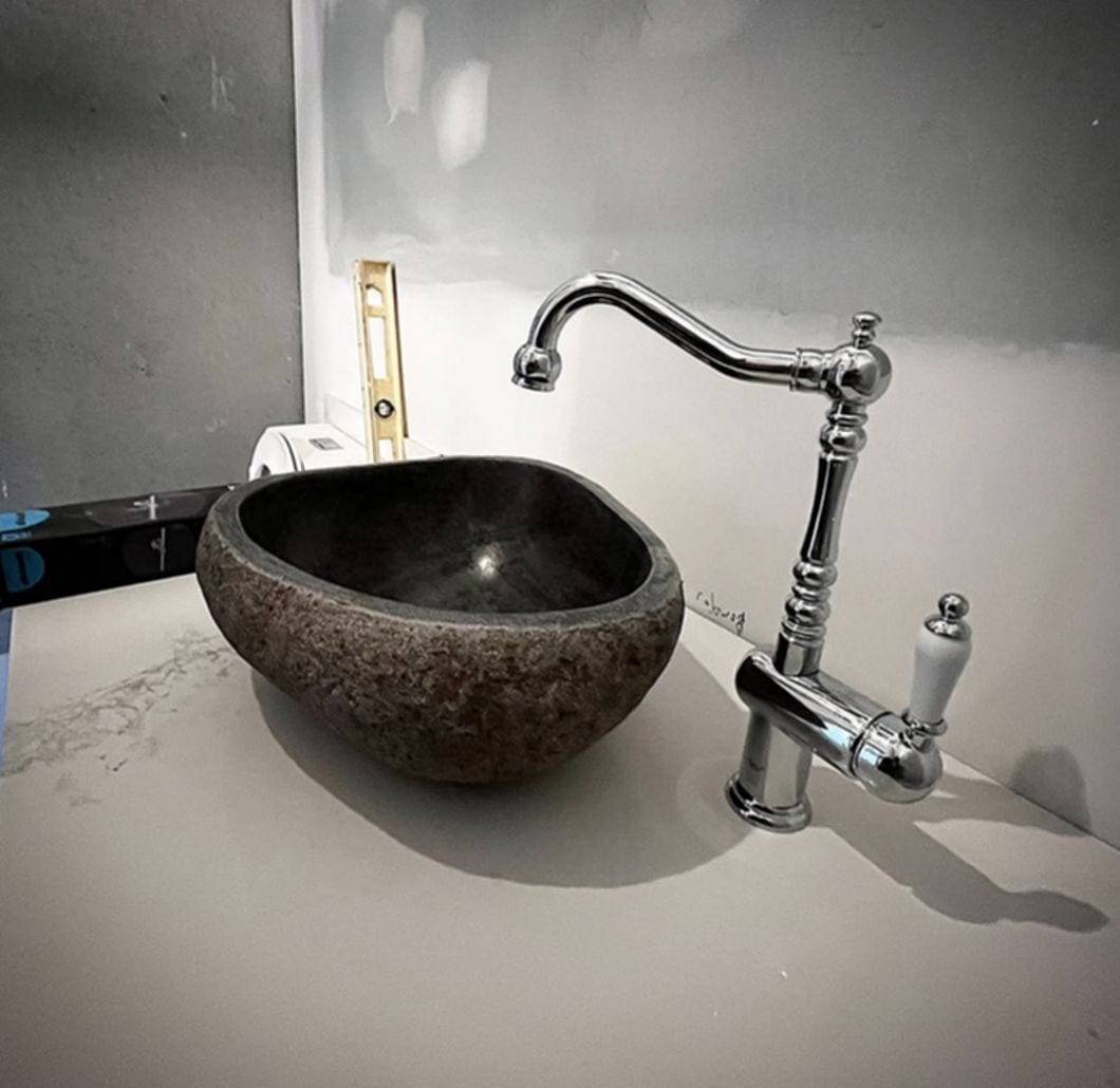 Round stone vessel sink on a white counter with a polished chrome gooseneck faucet and a white porcelain lever handle